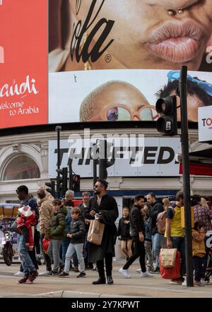 Londres, Angleterre, avril 30 2023 : les gens de Piccadilly Circus attendent de traverser la route dans une journée bien remplie avec les grands écrans derrière Banque D'Images