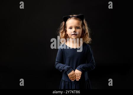 Fille drôle habillée comme chat pour la célébration d'Halloween sur fond noir Banque D'Images