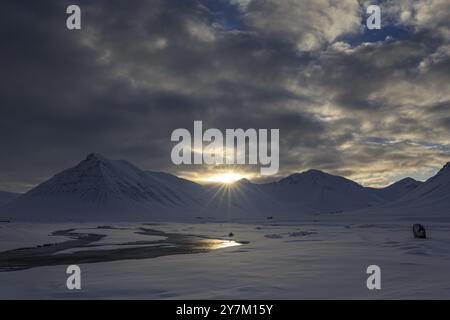 Lever de soleil sur la vallée avec rivière, étoile de soleil, nuages, neige, hiver, montagnes, Thingeyri, Westfjords, Islande, Europe Banque D'Images