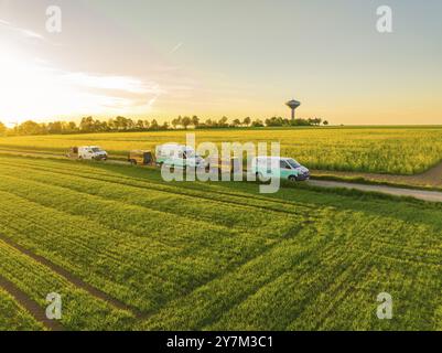 Voitures conduisant le long d'une route rurale à côté de champs verts et florissants au coucher du soleil, installation de fibre de verre, district de Calw, Forêt Noire, Allemagne, Europe Banque D'Images