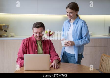Intéressé jeune couple heureux utilisant un ordinateur portable à la maison planifier facilement voyage en réservant via des applications en ligne. Banque D'Images