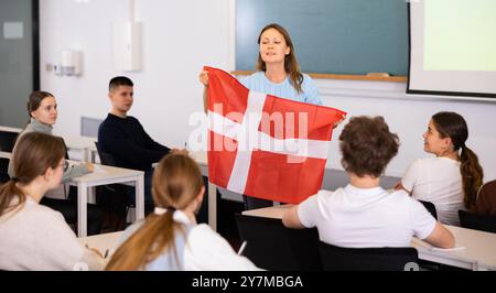 Un enseignant du secondaire parle aux élèves du Danemark et détient un drapeau du Danemark entre les mains. Banque D'Images