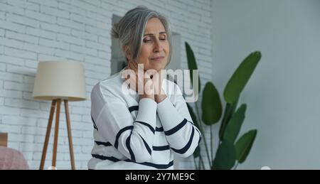 Femme âgée souffrant de mal de gorge alors qu'elle était assise sur le lit à la maison Banque D'Images