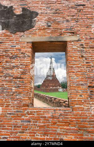 Vue d'une ancienne pagode dans un temple antique de la période Ayutthaya vu à travers une brèche dans le mur, des lieux historiquement importants. Banque D'Images