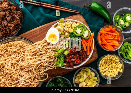 Nouilles ramen se déversant dans un bol de ramen de porc et de légumes : ramen garni d'un œuf dur, de piments forts, de carottes, d'oignons verts et d'épinards Banque D'Images