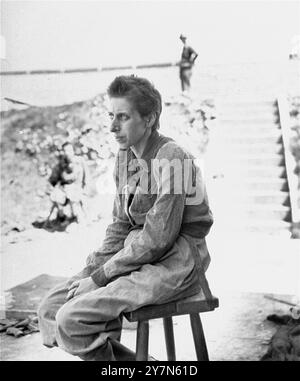 Une femme survivante pose dehors assise sur un tabouret dans le camp de concentration de Mauthausen nouvellement libéré. Mauthausen était un camp de travaux forcés nazi, faisant partie du complexe de Mauthausen. À son apogée, il y avait 85 000 prisonniers à la fois. Il était tristement célèbre pour sa dureté - on estime que sur les 190 000 prisonniers détenus pendant ses opérations, la moitié est morte. Il abritait la carrière de Wiener Graben et ses redoutables escaliers de la mort (Todessteige) où beaucoup moururent en transportant d'énormes charges sur les 186 marches de pierre. Banque D'Images