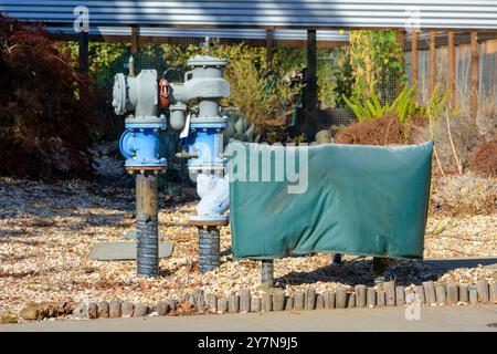 Paire de vannes d'eau industrielles et de tuyaux sont installés dans une zone paysagée avec du gravier et des plantes. Une unité est recouverte d'un cov vert résistant aux intempéries Banque D'Images