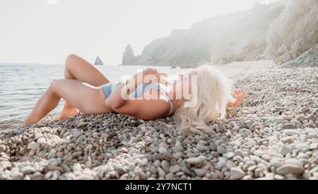 Femme blonde se relaxant sur une plage de galets Banque D'Images