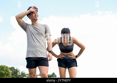 Un couple asiatique fatigué et en sueur en vêtements de sport essuie la sueur de leurs visages, prenant une pause après une longue course ensemble dans un parc le matin. c.a. extérieur Banque D'Images