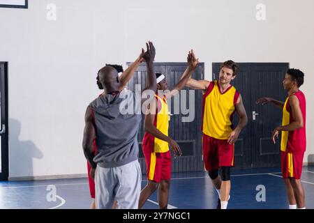 Coéquipiers talentueux, joueurs de basket-ball divers célébrant pendant l'entraînement dans la salle de gym de l'école Banque D'Images