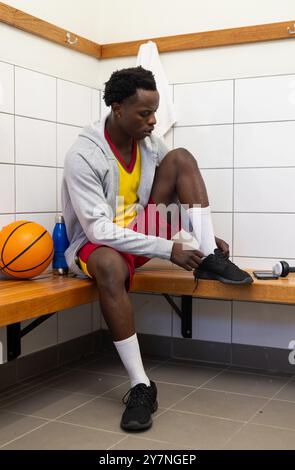 Lacets noués, joueur de basket-ball assis sur le banc dans le vestiaire avec balle Banque D'Images