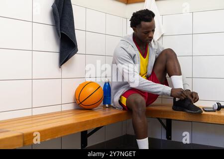 Lacets noués, joueur de basket-ball assis sur le banc dans le vestiaire avec balle, espace de copie Banque D'Images