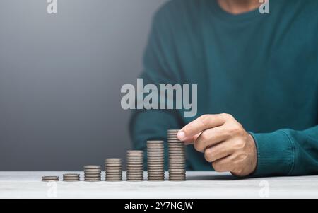 L'homme empile des pièces sur une table, les arrangeant de la plus petite à la plus grande. L'image représente la croissance financière, l'épargne et des gestionnaires d'argent prudents Banque D'Images