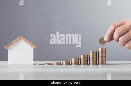 L'homme empile des pièces sur une table, les arrange du plus petit au plus grand, avec un modèle de maison en bois à côté de lui. Met l'accent sur le concept de sauver Mone Banque D'Images