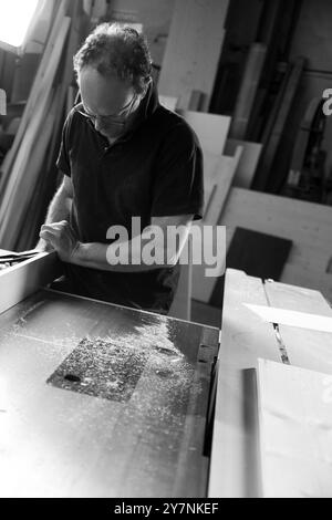 L'image en noir et blanc d'Un charpentier utilise une raboteuse à bois dans son atelier, entourée de bois et d'outils Banque D'Images