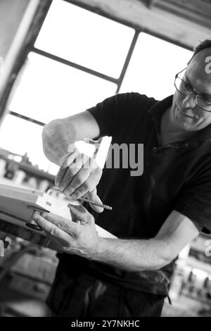 Image en noir et blanc d'un menuisier qualifié à l'aide d'un ciseau dans un atelier confortable, fabriquant du bois avec précision. Capture le dévouement et la concentration dans la menuiserie Banque D'Images