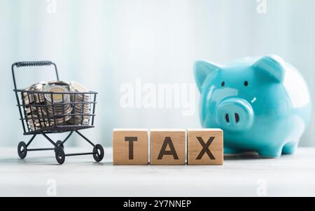 LA TAXE est écrite sur un bloc de bois et des pièces de monnaie dans un panier sur une table en bois sur un fond blanc brillant. Taxe commerciale et planni financier Banque D'Images