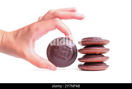 Cueillette à la main un biscuit au chocolat à côté d'une pile de biscuits similaires sur un fond blanc propre, mettant l'accent sur le choix de collation. Banque D'Images