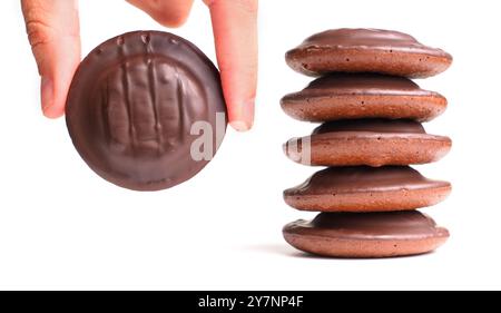 Main tenant un biscuit au chocolat à côté d'une pile de biscuits recouverts de chocolat sur un fond blanc, soulignant la délicatesse. Banque D'Images