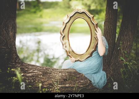 femme tenant un miroir reflétant la nature derrière, concept abstrait Banque D'Images