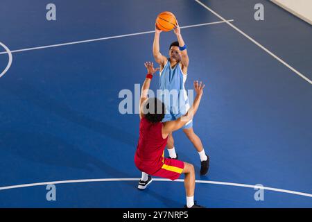 Jouant au basket-ball, deux hommes en vêtements de sport en compétition sur un terrain couvert Banque D'Images