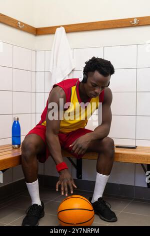 Écouter de la musique avec des écouteurs, joueur de basket-ball assis dans le vestiaire Banque D'Images