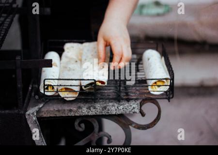 Cuisiner en plein air. Une femme cuisine des tortillas pita sur un feu de barbecue extérieur. Préparation végétarienne des aliments BBQ. Rouler à la main des emballages de légumes. Banque D'Images