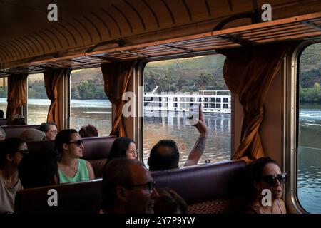 Pinhão, Portugal - 5 octobre 2023 : le fleuve Douro et le bateau de croisière vus à travers les fenêtres d'un wagon de train de passagers sur la ligne du Douro au Portugal w Banque D'Images