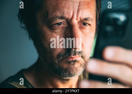 Gros plan d'homme adulte mature regardant le téléphone mobile à l'intérieur avec l'attention au contenu affiché à l'écran, mise au point sélective Banque D'Images