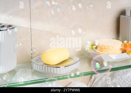 Gros plan de la barre de savon sur l'étagère en verre dans la salle de bain avec des bulles de savon tombant Banque D'Images