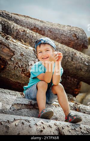 Un petit enfant dans une casquette de baseball bleu denim shorts courts et s'assied sur un journal et rit joyeusement Banque D'Images