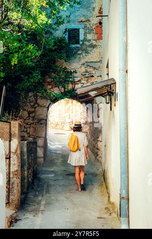 Fille touriste marchant à travers l'ancienne rue étroite sur une belle journée d'été dans la ville d'Omisalj, Croatie. Banque D'Images