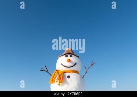 Bonhomme de neige drôle dans un chapeau jaune élégant et une écharpe jaune. Ciel bleu clair sur fond Banque D'Images