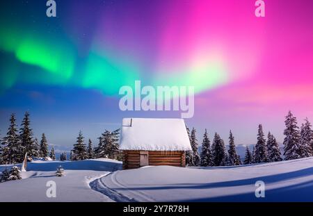 Paysage de Noël de fées avec lumière du Nord violet sur cabane en bois dans la forêt enneigée. Scène d'hiver avec lumière polaire dans les montagnes gelées. Aurora Borealis Banque D'Images