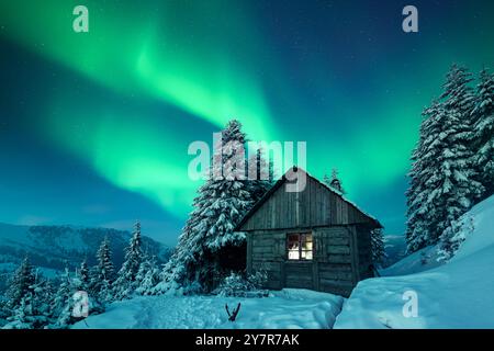 Paysage de Noël de fées avec lumière du Nord sur cabane en bois dans les montagnes enneigées. Scène hivernale avec lumière polaire. Aurora Borealis Banque D'Images