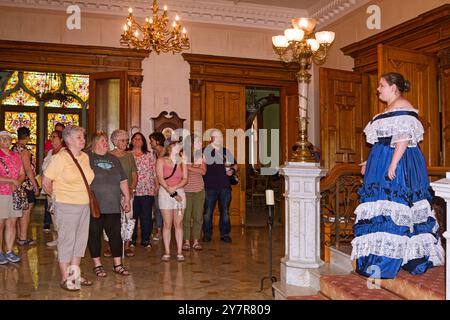 Guide touristique bénévole, en longue robe à volants, bleu avec dentelle blanche, parlant à un groupe de personnes, cadre élégant, ancien manoir de Pott, Langoma, 1897, bonjour Banque D'Images