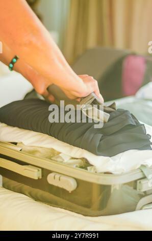 la femme âgée emballant des vêtements dans une valise orange ouverte sur un lit. . Photo de haute qualité Banque D'Images