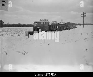 LES NEIGES COUPENT LES VILLAGES... BLOQUEZ D'AUTRES ROUTES. ENCORE LE THERMOMÈTRE TOMBE 1.2.54 le Grand froid continue sans signe de rupture, les rapports indiquent que la mer est gelée à Southend et un certain nombre de villages sont coupés de leurs approvisionnements. Des gangs de bénévoles et des chasse-neiges ont été amenés à aider aux secours. Un de ces villages était Eastling, Kent, où nos photos ont été prises. I.N. photo montre : un convoi de transport transportant des fournitures essentielles au village coupé, suit un chasse-neige qui fait une voie à travers la neige. Photo de R. Palmer. TDH/74310 ACTUALITÉ INTERNATIONALE PHOT Banque D'Images