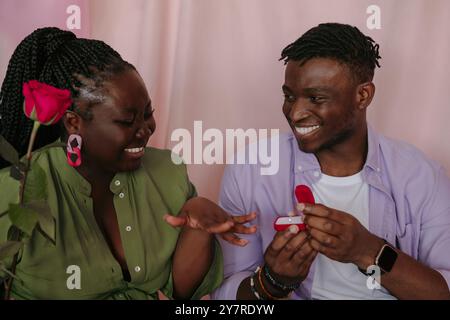 Homme africain romantique donnant bague de fiançailles à sa petite amie tout en faisant une proposition sur fond rose Banque D'Images