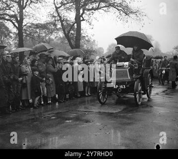 Course automobile annuelle vétéran. 1.11.53. La voiture de longue date qui reliait Londres à Brighton est partie ce matin de Hyde Park, sous de fortes pluies. La course a commencé en 1896, et il y avait plus de 180 voitures inscrites. INP photo montre Mr. ici avec son millésime 6 hp MMC 1899 trouve son grand parapluie très utile au départ de la course depuis Hyde Park ce matin, regardé par quelques passionnés robustes. Photo de J. Waldorf. EM 72266. Photos d'actualités internationales. Banque D'Images