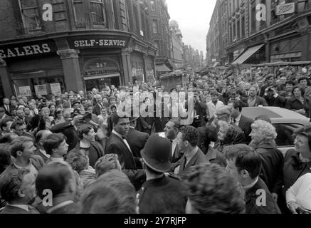 LONDRES : deux gendarmes de police tentent vigoureusement de retenir la foule dans la rue Brewer Soho aujourd'hui, où l'américain Muhammad Ali (au premier plan face à la caméra), le champion du monde de boxe poids lourds tentait de quitter une conférence de presse qu'il donnait dans le restaurant voisin d'Isow. Clay, qui rencontre le champion poids lourd britannique et de l'Empire Henry Cooper à Highbury le 21 mai, a déclaré lors de la conférence de presse qu'il faisait tout pour être un champion digne. Le champion, maintenant doux, doux et mature, remercia tous les intéressés de lui avoir donné le temps nécessaire pour visiter la Grande-Bretagne et se défendre contre Cooper pour le cha Banque D'Images