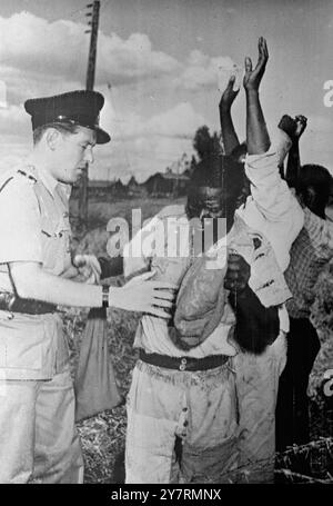 TOP MAU DIRIGEANTS MAU PRIS DANS UN GRAND COUP À NAIROBI 6.10.53. Plus de 500 policiers et soldats ont arrêté hier un dirigeant de haut rang de Mau Mau et quatorze autres terroristes lors de raids de masse à Nairobi, la capitale du Kenya. Deux compagnies des Royal Inniskill Fusiliers, à baïonnettes fixes, prennent part au raid. Les hommes et les femmes arrêtés ont défilé vers des points de collecte centraux où des équipes de contrôle composées d'Africains et d'Européens ont examiné les laissez-passer et cherché des armes. I.N.P. PHOTO MONTRE : un officier des West African Rifles fouille un suspect Mau Mau à la recherche d'armes dissimulées. D'autres suspects avec les bras se lèvent Banque D'Images