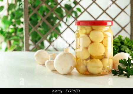 Savoureux champignons marinés dans le pot et le persil sur la table blanche à l'intérieur, espace pour le texte Banque D'Images