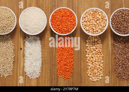 Différents types de céréales et de légumineuses dans des bols sur une table en bois, pose à plat Banque D'Images