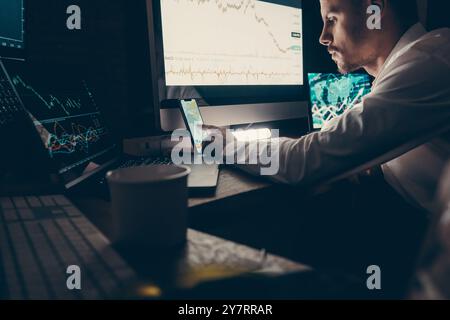 Commerçant boursier masculin utilisant des technologies tout en analysant des graphiques et des graphiques dans le bureau de nuit Banque D'Images