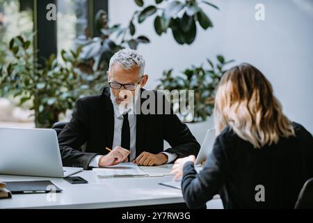 Homme mûr confiant en vêtements de forme interrogeant le candidat à l'emploi tout en étant assis au bureau dans le bureau Banque D'Images