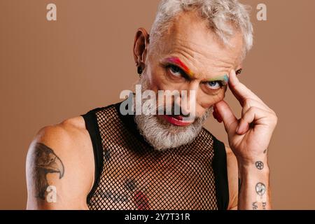 Portrait d'homme gay mature barbu avec des sourcils colorés arc-en-ciel debout sur fond brun Banque D'Images