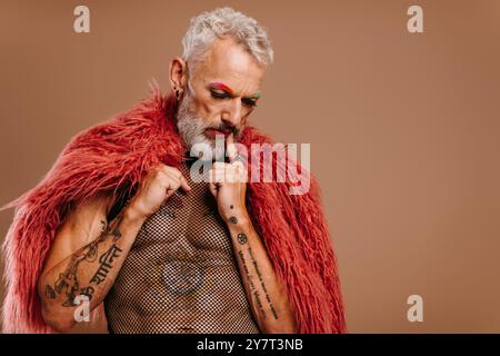 Portrait d'homme gay mature avec des sourcils colorés arc-en-ciel portant un manteau moelleux sur fond brun Banque D'Images
