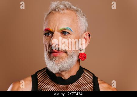 Portrait d'homme gay mature barbu avec des sourcils colorés arc-en-ciel sur fond brun Banque D'Images