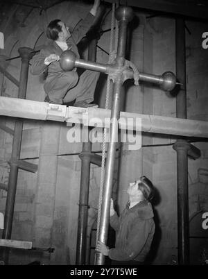 ASCENSION DE LA CROIX la croix de 9 pieds de haut qui surmontera la flèche restaurée dans la cathédrale de Salisbury est facilitée par la chambre de l'horloge par le steeplejack Richard Burford de Londres. La croix est en métal résistant aux acides non ferreux, le revêtement en bronze a été fait à Londres. Les ouvriers ont restauré les 27 pieds supérieurs de la flèche de la cathédrale de Salisbury, qui s'élève à 404 pieds dans le ciel. La pierre corrodée a été remplacée. 5 décembre 1950 Banque D'Images